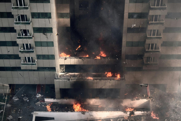 A large, multi floor building on fire with large plumes of smoke and ash